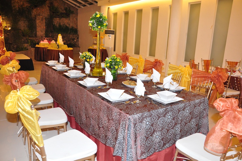 Table setup with flower arrangements, yellow and orange ribbons in chairs